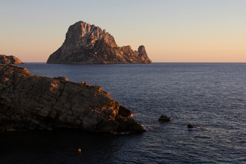 Es Vedrà at sunset, with a sailboat passing in the foreground.